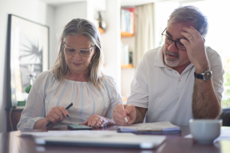 Older couple reviewing paperwork and making notes together at a table