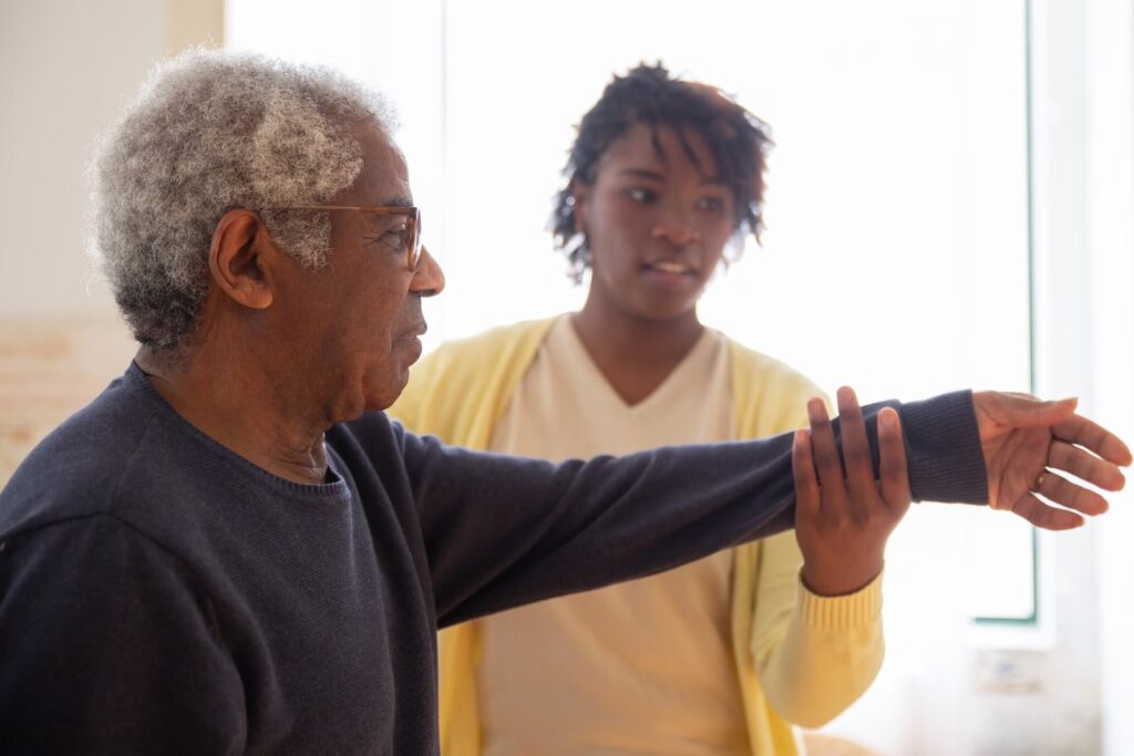 Caregiver helping an older man with arm exercises.