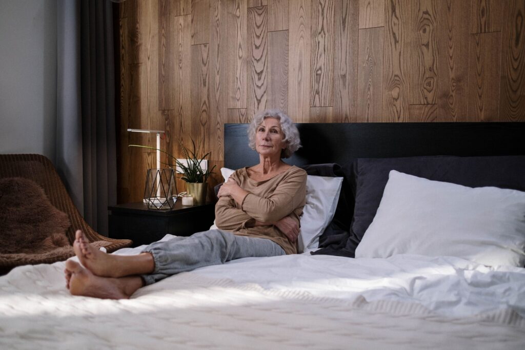 Older woman sitting awake against pillows on her bed.